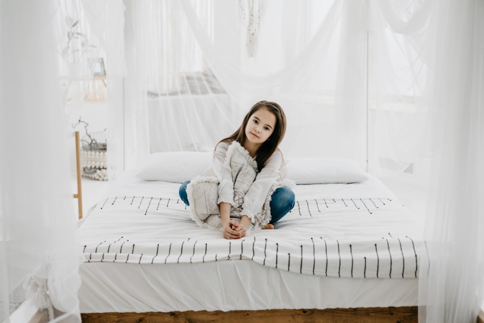 Młoda kobieta w jasnym, minimalistycznym pokoju siedzi na łóżku z ekologicznym materacem, co symbolizuje harmonię i naturalne materiały.